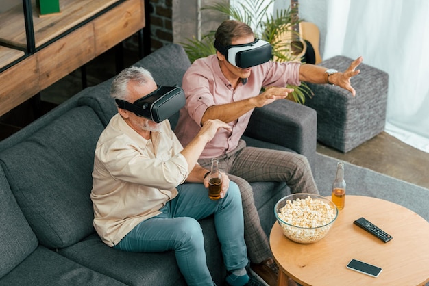 high angle view of mature male friends drinking beer and using virtual reality headsets