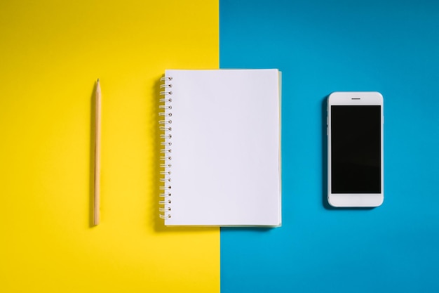 High angle view of mobile phone with note pad and pencil over colored background