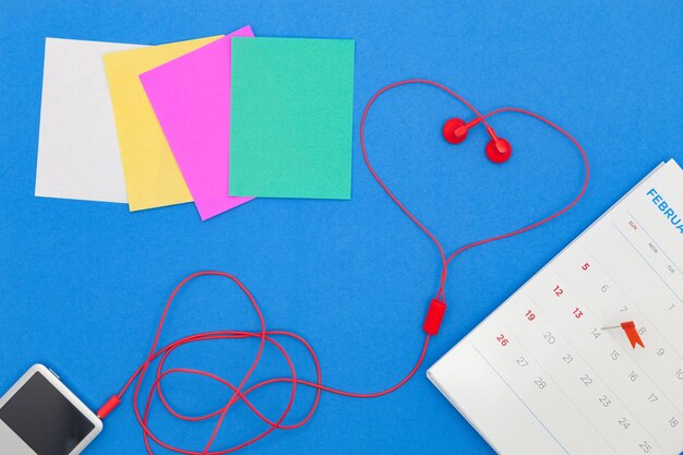 High angle view of mp3 player with calendar and colorful papers over blue background