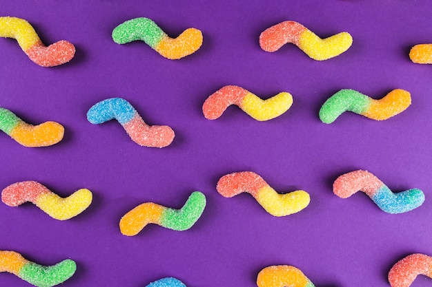 High angle view of multi colored gummy worm candies on purple surface