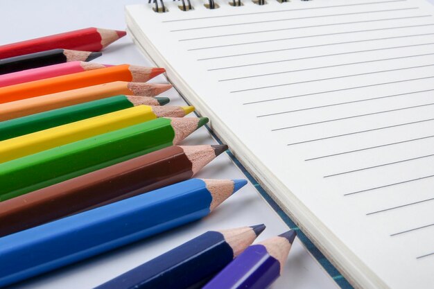 High angle view of multi colored pencils with spiral notepad on table