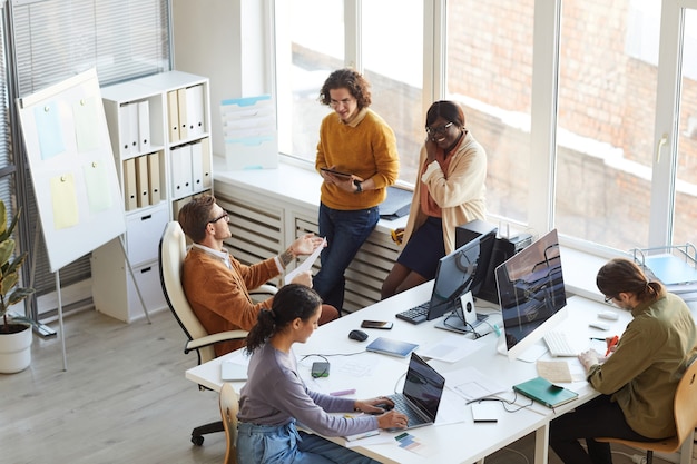 High angle view at multi-ethnic IT development team collaborating on business project while working in software production studio, copy space