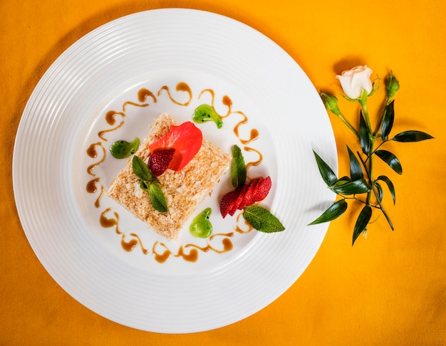 Foto vista ad alta angolazione della torta napoleon con fragole servite in piatto da una rosa sul tavolo