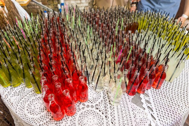 Высокий угол обзора изысканных газированных напитков в прозрачных стеклянных бутылках с трубочками для питья, упорядоченными по цвету на столе на мероприятии