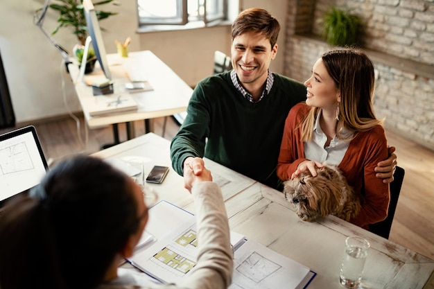 写真 オフィスでの会議に成功した後の不動産業者との犬のハンドシェークと幸せなカップルの高角度のビュー