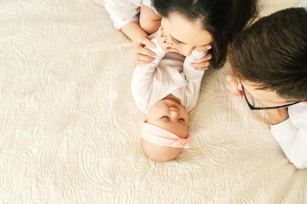 写真 ベッドに横たわっている赤ちゃんの女の子と遊んでいる両親のハイアングルビュー
