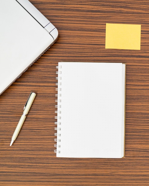 Фото Высокоугольный вид ручки и блокнота с липкой запиской и ноутбуком на коричневом столе