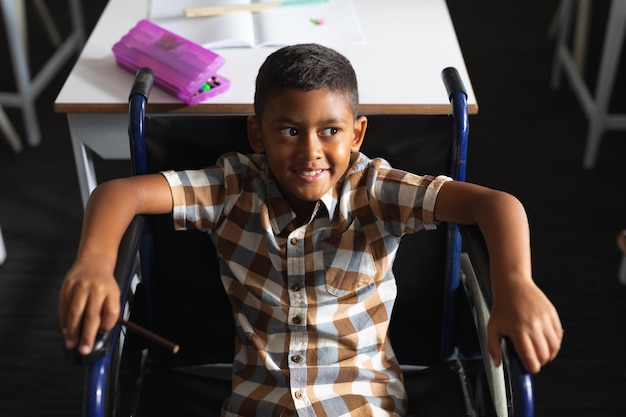 Фото Высокоугольный вид улыбающегося двухрасового мальчика, сидящего в инвалидном кресле в классе