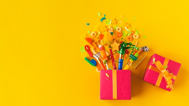 High angle view of open gift box with candies and party accessories on yellow surface