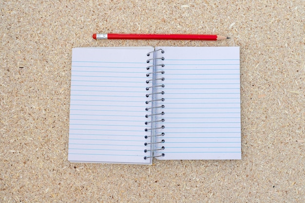 High angle view of an open spiral blank notebook with pencil on a cork board background