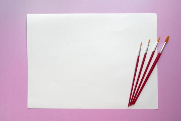 Photo high angle view of paper and paintbrushes on pink background