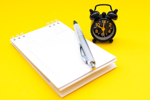 High angle view of pen by book with clock on yellow background