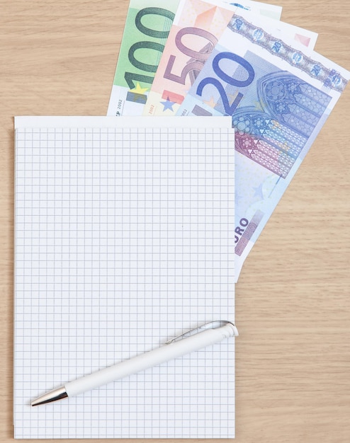 Foto vista ad alto angolo della penna e del blocco banconote con varie banconote in euro sul tavolo