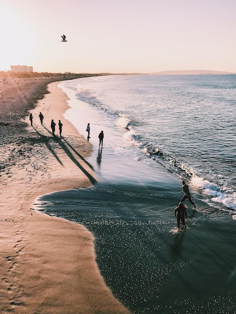 High angle view of people enjoying at beach against sky during sunset