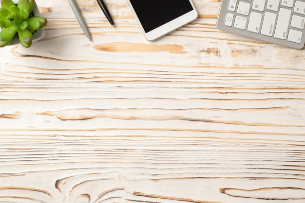 Above high angle view photo of office supplies computer keyboard flowerpot and telephone isolated white wooden backdrop with copy blank space