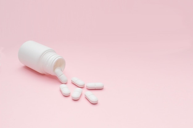 High angle view of pills spilling from bottle against pink background