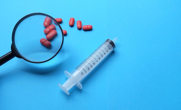 High angle view of pills and syringe against blue background