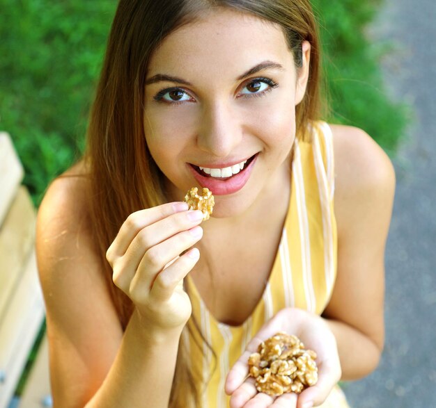 Foto ritratto ad alto angolo di una donna che mangia noci mentre è seduta su una panchina al parco