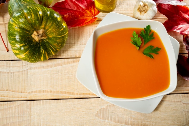 Vista dall'alto della zuppa di zucca servita in una ciotola con foglie autunnali sul tavolo.