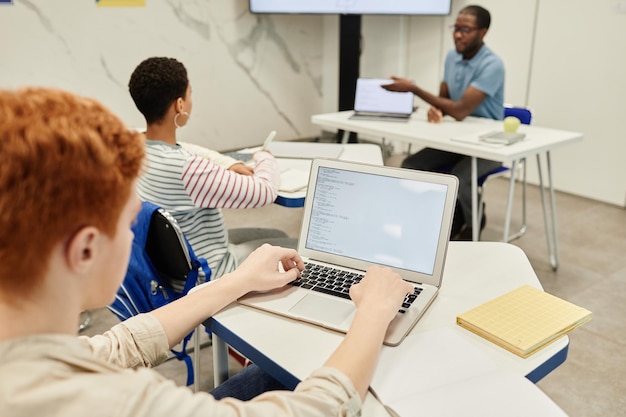 Высокий угол обзора рыжеволосого подростка, использующего ноутбук в классе кодирования для детей, пространство для копирования