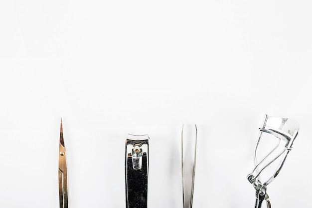 Photo high angle view of scissors; nail clipper; tweezer and eyelash curler on white backdrop