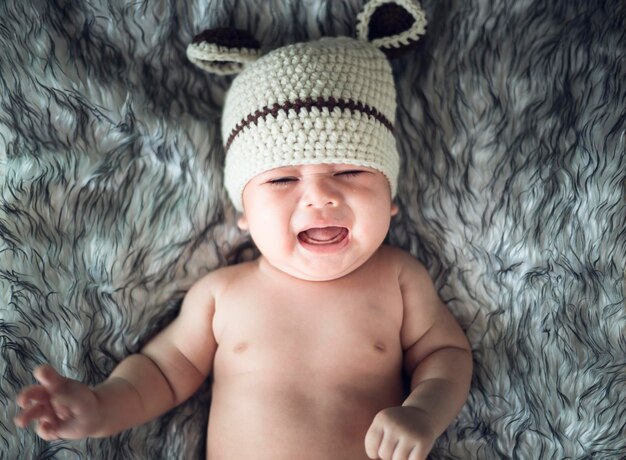 Photo high angle view of shirtless baby girl crying while lying on bed