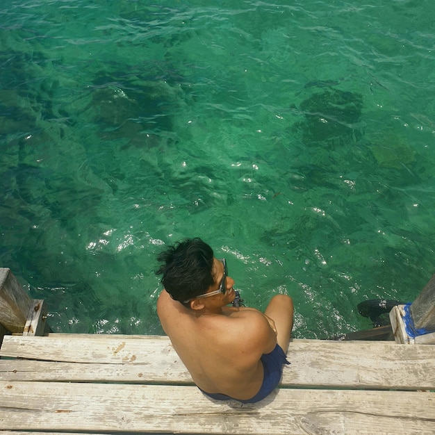 High angle view of shirtless mid adult man sitting on pier over lake