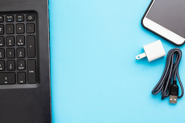 Photo high angle view of smart phone with cable and laptop against blue background