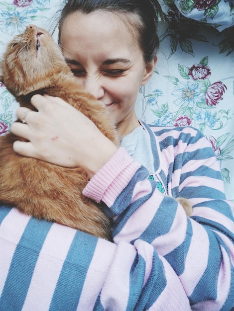 Foto vista ad alta angolazione di una donna sorridente che abbraccia un gatto sul letto