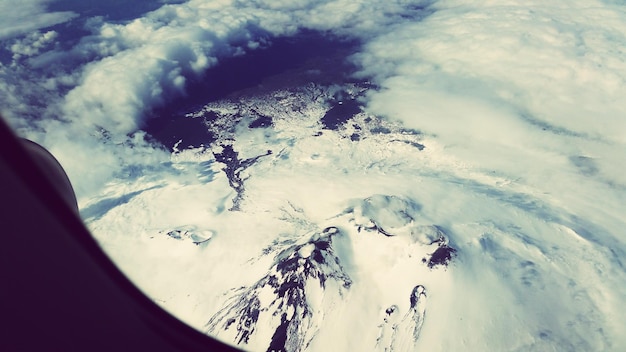 Foto vista ad alta angolazione delle montagne coperte di neve viste attraverso la finestra dell'aereo