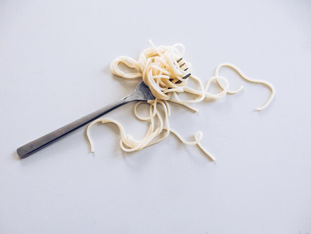 Высокоугольный вид спагетти на вилке на белом фоне