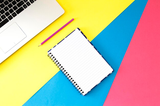 high angle view of spiral notebook and laptop on colored background