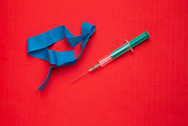 High angle view of syringe and resistance band on red background