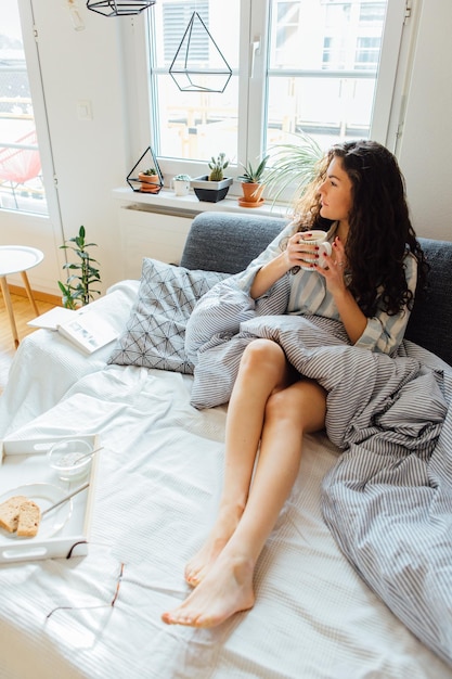 家でベッドでコーヒーを飲んでいる間 ⁇ 考え深い若い女性のハイアングルビュー