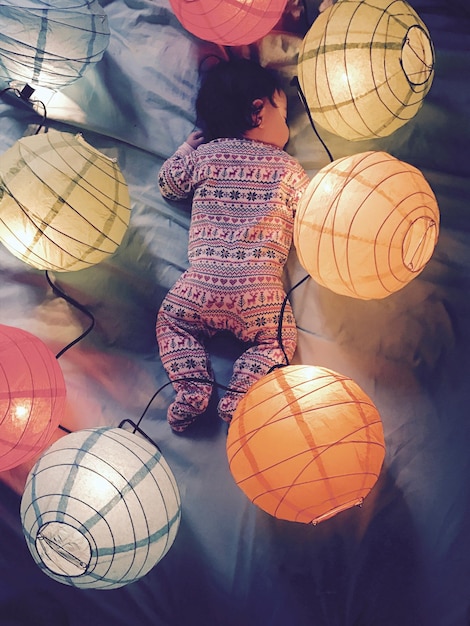 Photo high angle view of toddler sleeping amidst illuminated lanterns on bed