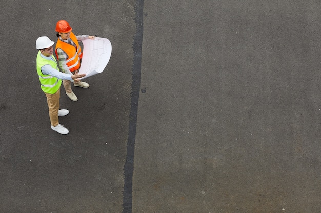 High angle view of two engineers standing outdoors and examining the blueprint of new project