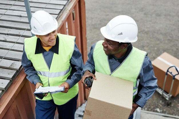 Photo high angle view at two smiling workers carrying boxes up stairs at shipping docks