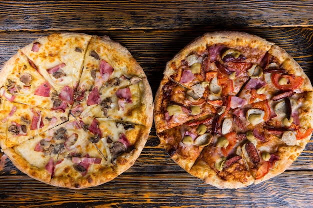 High angle view of two tasty different pizzas with variety of toppings and cheese on wooden table