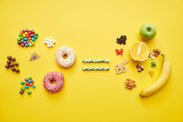 High angle view of unhealthy candies and sweet doughnuts being equated with fresh and dried fruits o