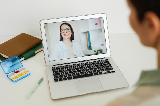 High angle view at unrecognizable woman talking to female doctor on laptop screen by video chat during online consultation, copy space