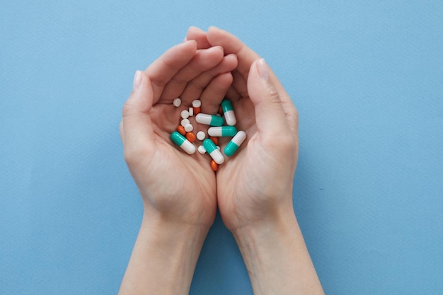 High angle view of unrecognizable woman with handful of pills against blue background