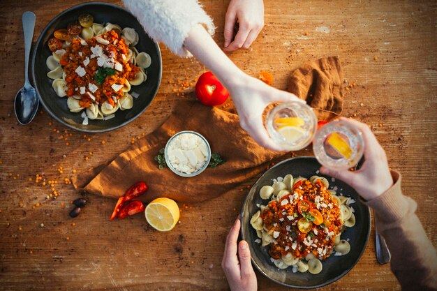 Photo high angle view of vegetarian lentil bolognese with orecchiette on table and people holding drinks