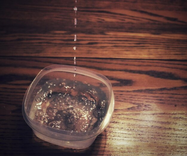 High angle view of water dripping in bowl on wooden table