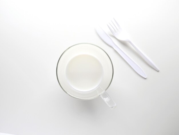 Высокоугольный вид белой чашки и белых приборов на столе на белом фоне
