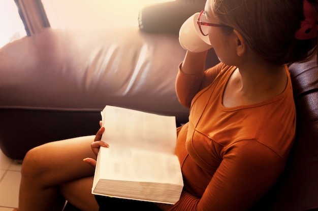 Foto vista ad alta angolazione di una donna che legge un libro mentre beve caffè a casa