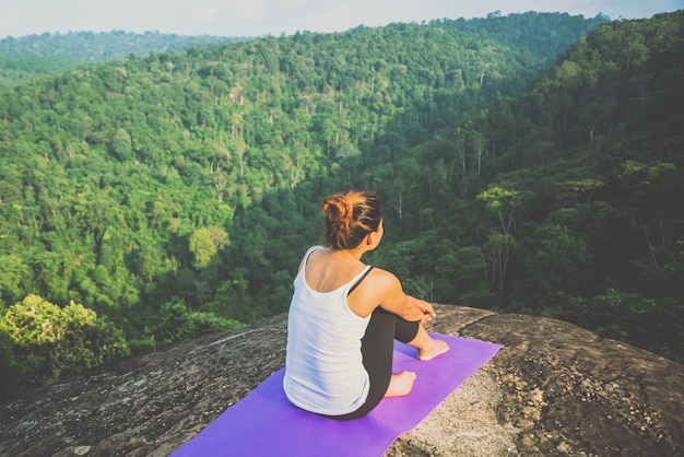 High angle view of woman sitting on exercise mat on cliff against landscape