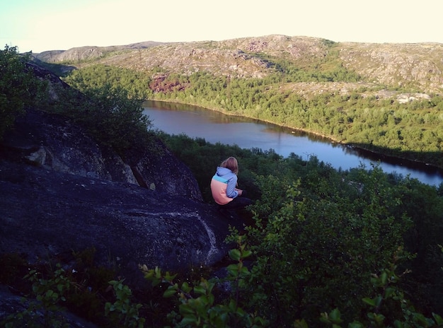 Foto vista ad alto angolo di una donna seduta su una roccia vicino al lago contro il cielo