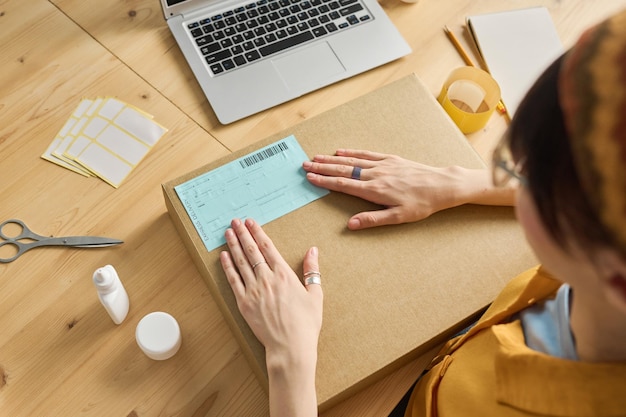 High angle view of woman sticking receipt on parcel at table\
before shipping