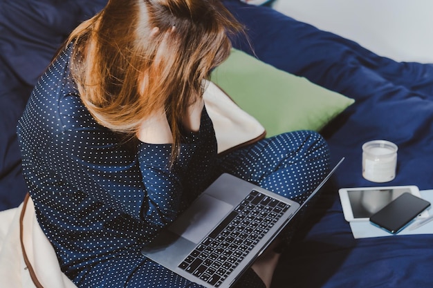 High angle view of woman using laptop while sitting on bed