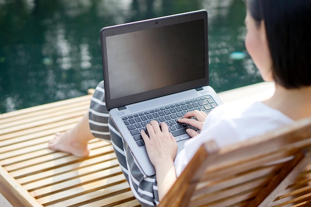 수영장  의자 에 앉아 있는 여자 가 노트북 을 사용 하고 있는 높은 각도 의 모습
